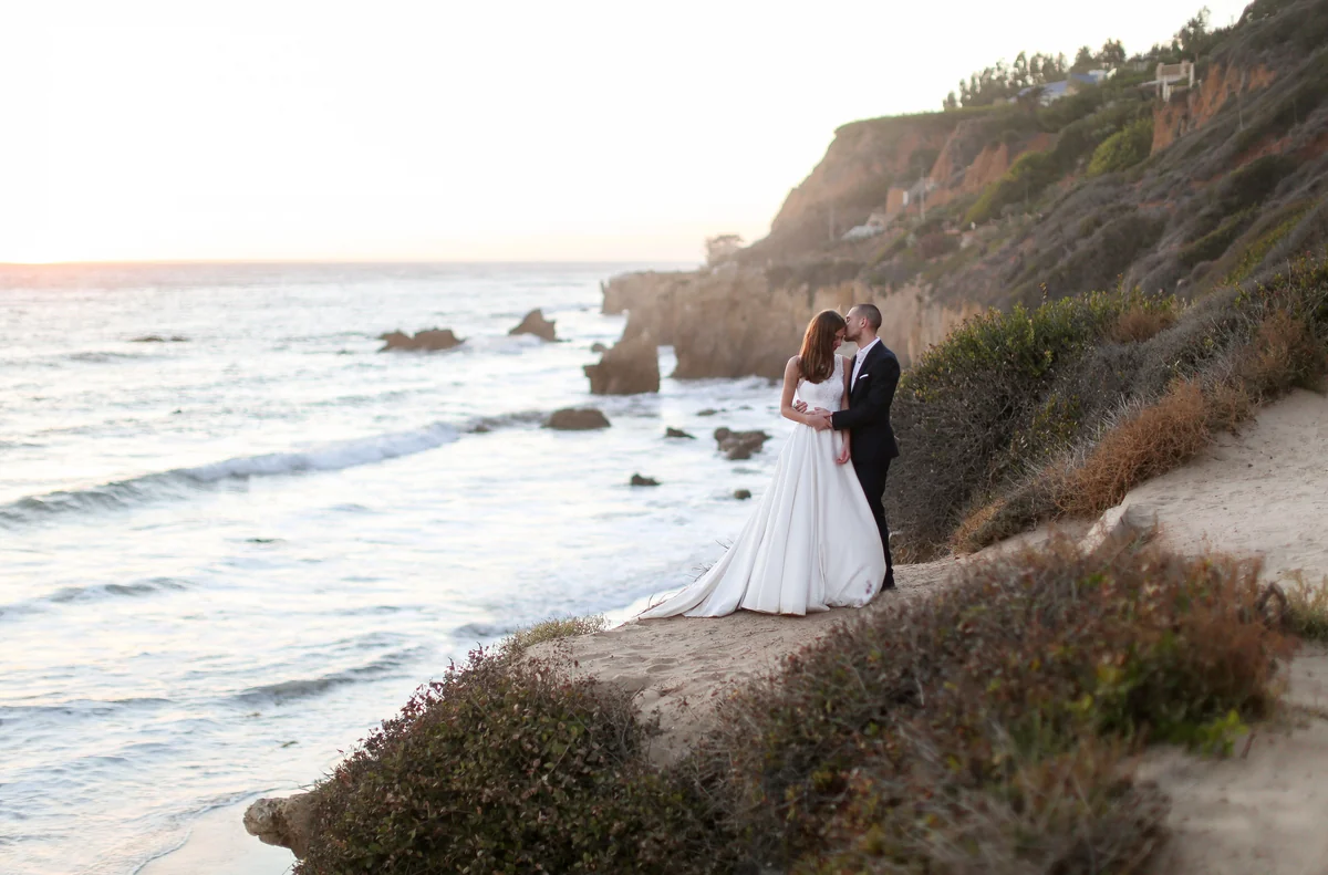 A wedding couple on a quiet cliff above the ocean at sunset