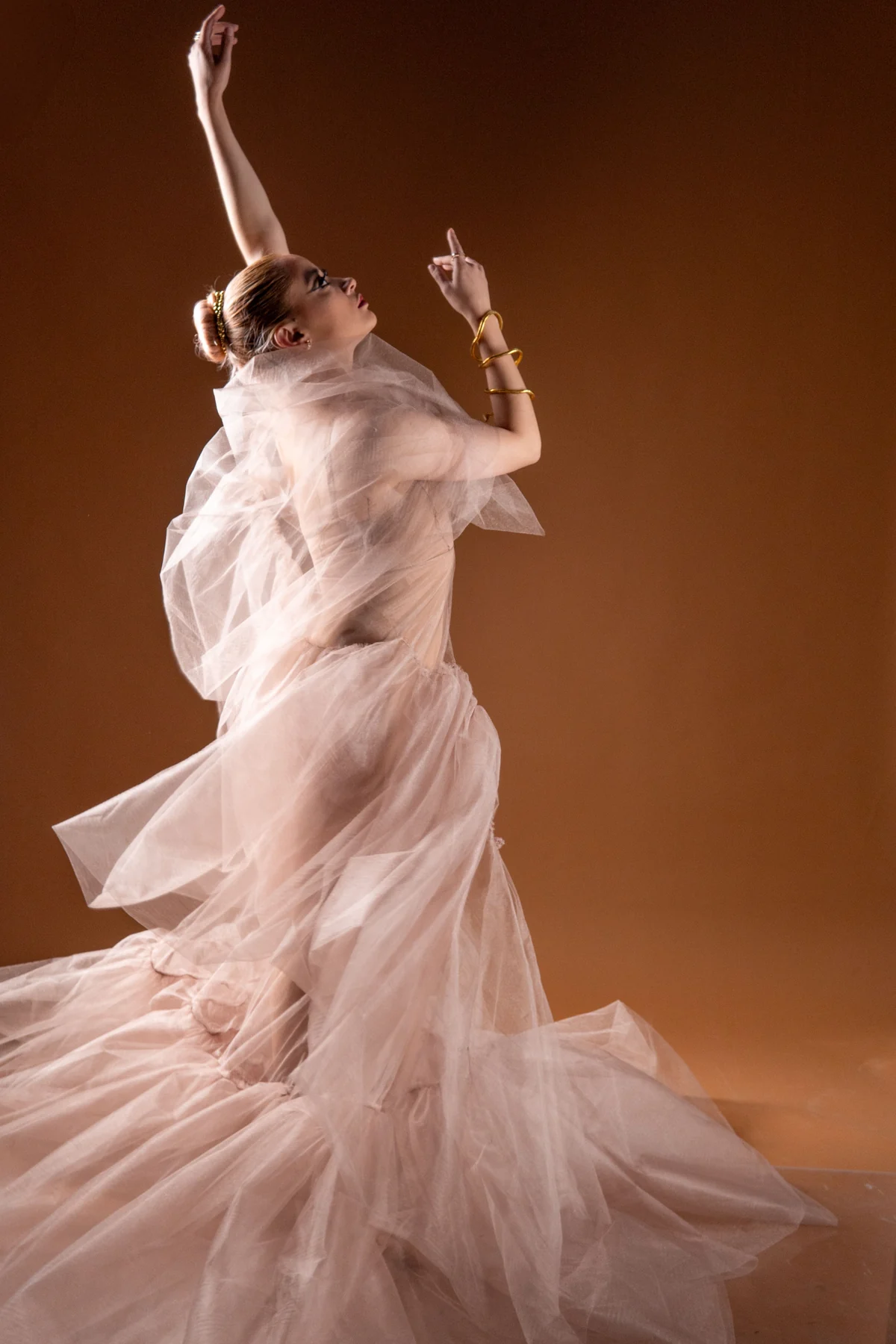 A dancer reaching into the light in flowing blush fabric